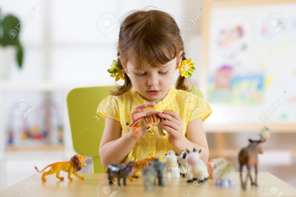 child girl playing with animal toys at table in kindergarten or home